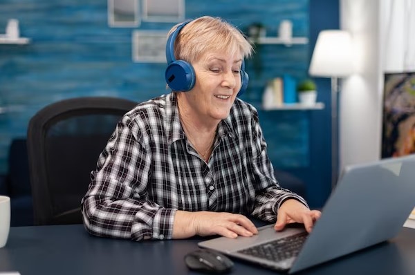 old woman listing music and using laptopp
