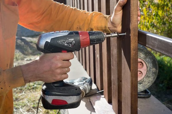 person repaire wood fence with machine