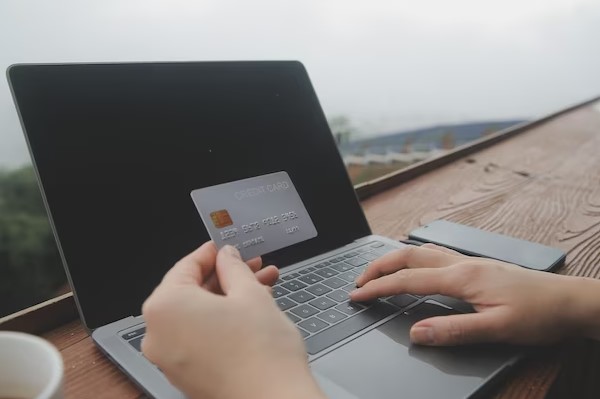 person hand holding debit car and usnig laptop