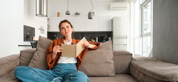 girl sitting on sofa holding a book with air conditioner house